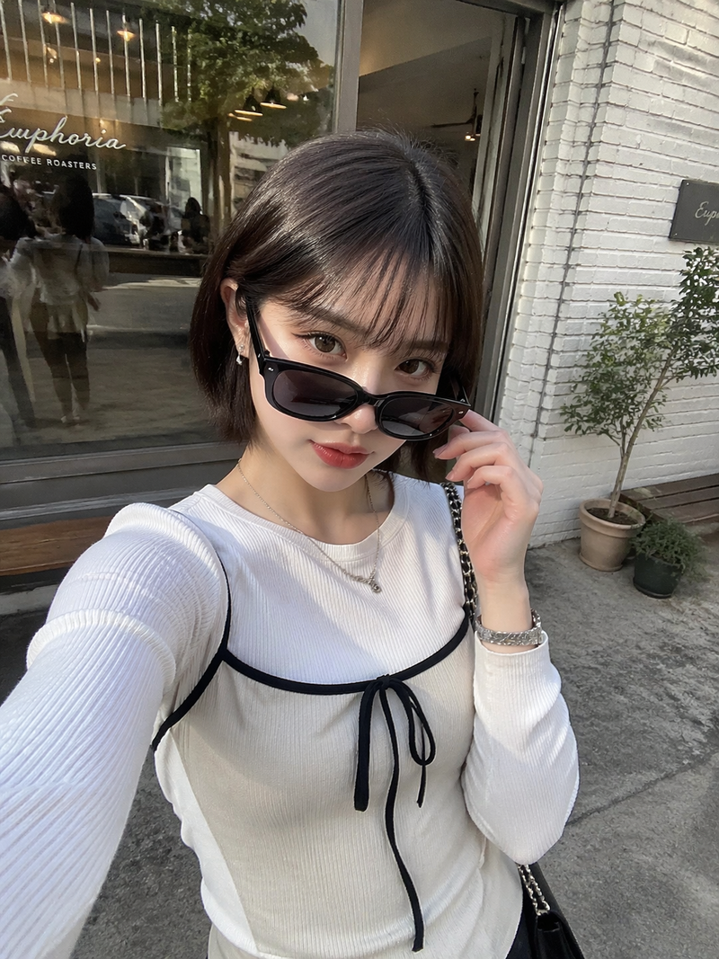日本の若い20代の女性がカフェの前でiPhoneで自撮りした写真。ファッションは韓国風ファッション、ショートボブ、サングラスを少し下げてカメラを見ている。